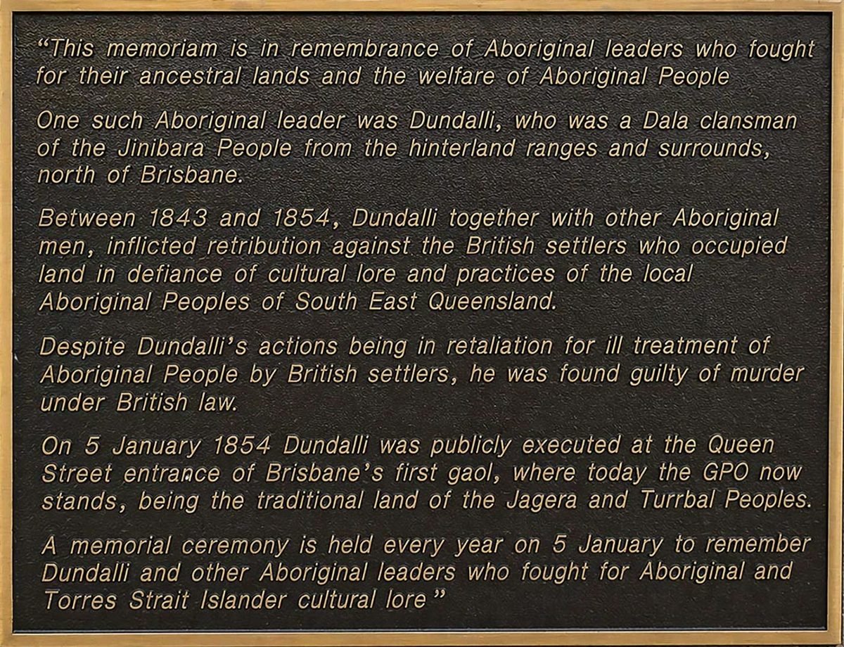 Bronze memorial plaque to Aboriginal leader Dundalli at the Brisbane GPO, with raised gold lettering on a dark patinated background, set into a stone surround.