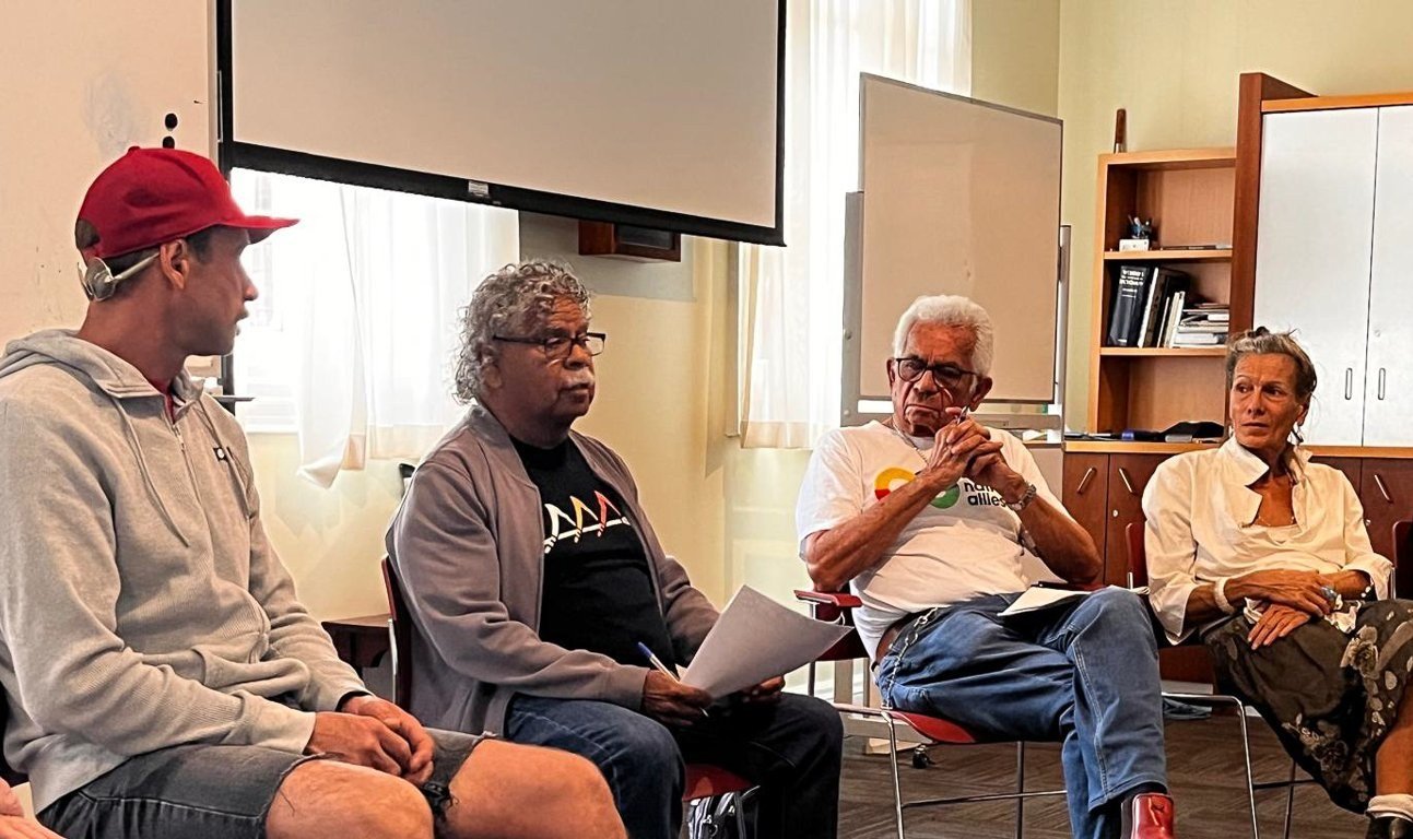 Four participants sit in a row in the Darnell Room, including Uncle Billy Gorham (second from left) holding his notes, and Uncle Bill Lemson (third from left) listening with hands clasped.