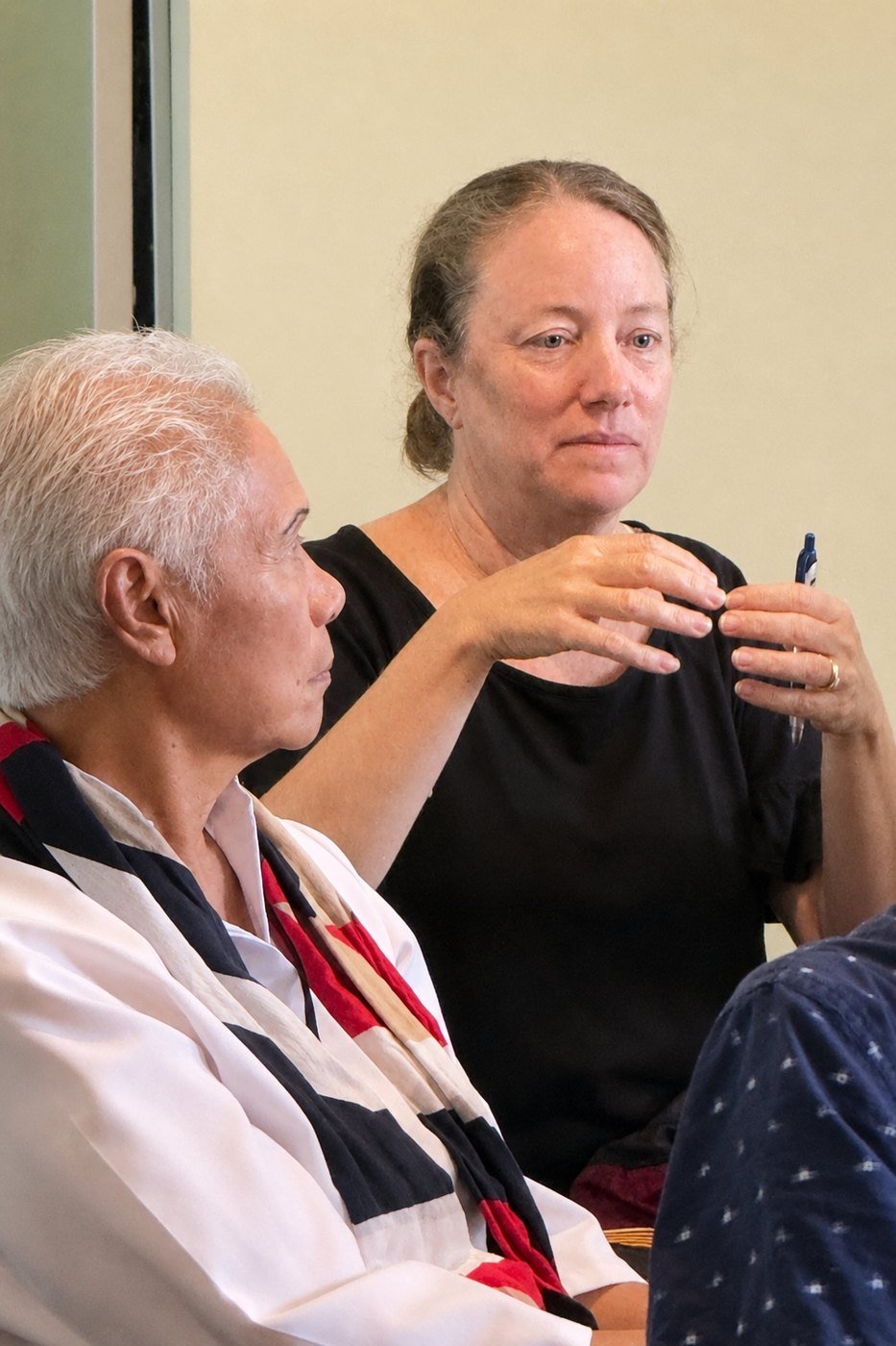 A participant in the circle speaks, pen in hand, while another listens in the foreground.