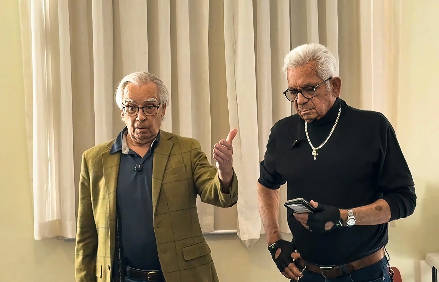 Colin Thomas standing mid-story, gesturing as he speaks, with Uncle Bill Lemson beside him in the Darnell Room