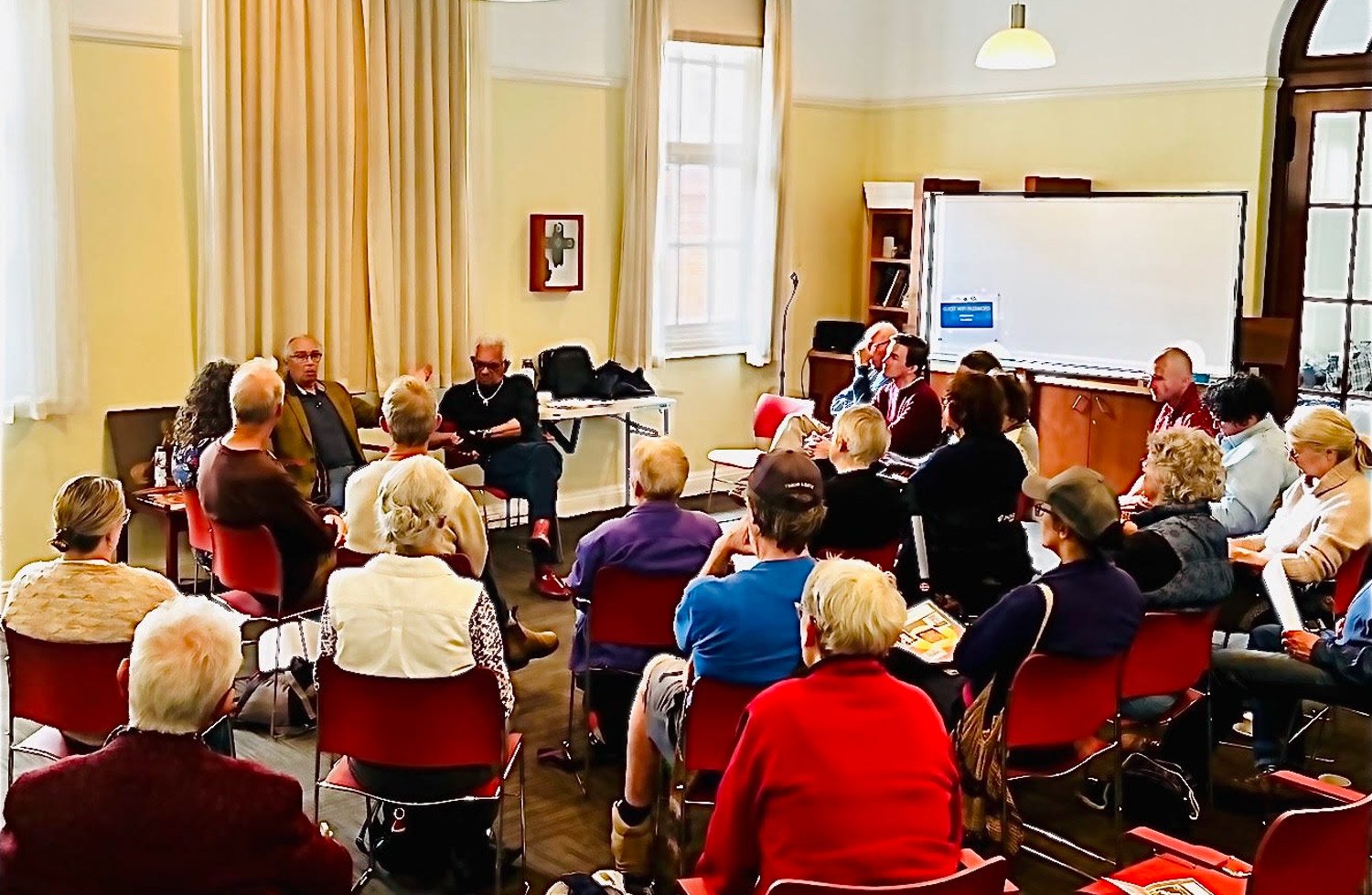 The Yarning Circle in session in the Darnell Room: two dozen people seated in a circle of red chairs, listening